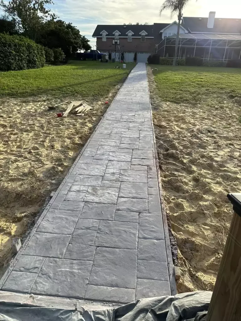 Gray stamped concrete walkway running across a sandy yard toward a house, Sugarmill Woods, FL